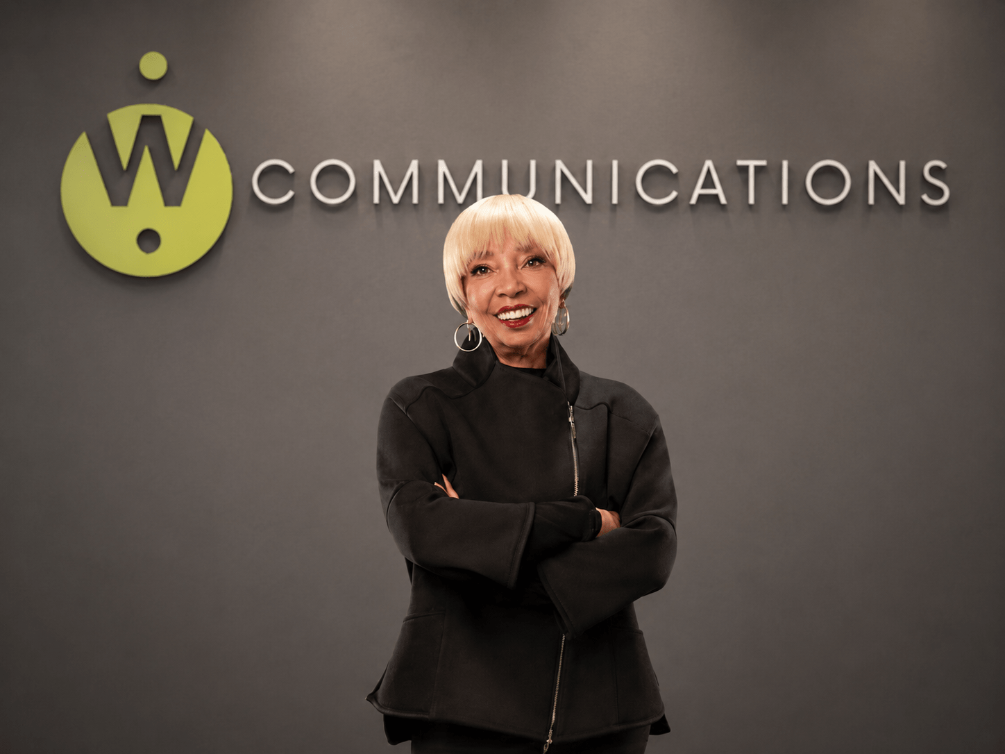 Wanda J. Herndon at the W Communications office, standing before the company logo